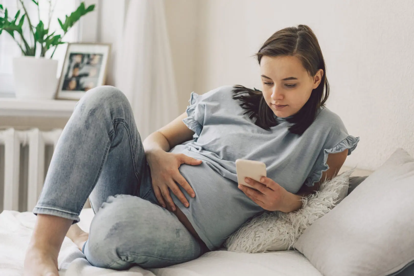 Pregnant woman using phone on bed.