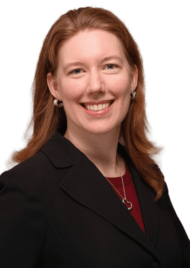 Woman in black blazer with heart necklace.