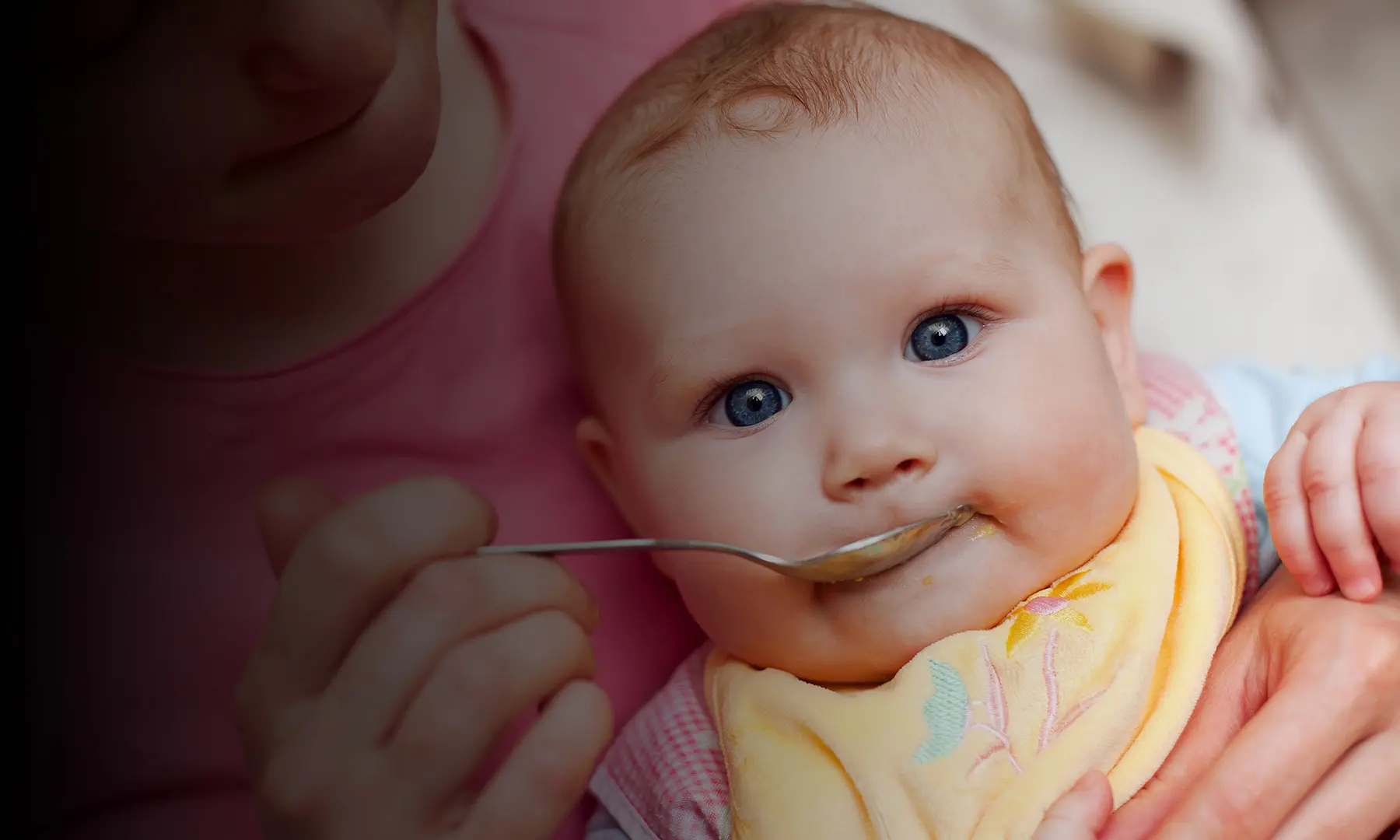 Caucasian mom feeding her infant baby with spoon