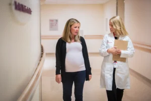 Doctor holding clipboard walking with expectant mother