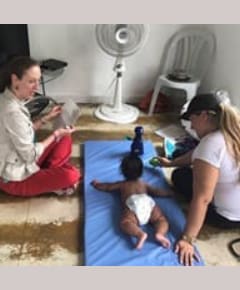 Two adults interacting with baby on blue mat