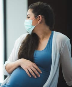 Pregnant woman wearing face mask looking out window