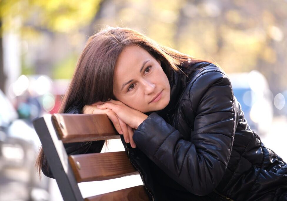 Young Sad Woman Sitting Alone On Street Bench Outdoors Thinking