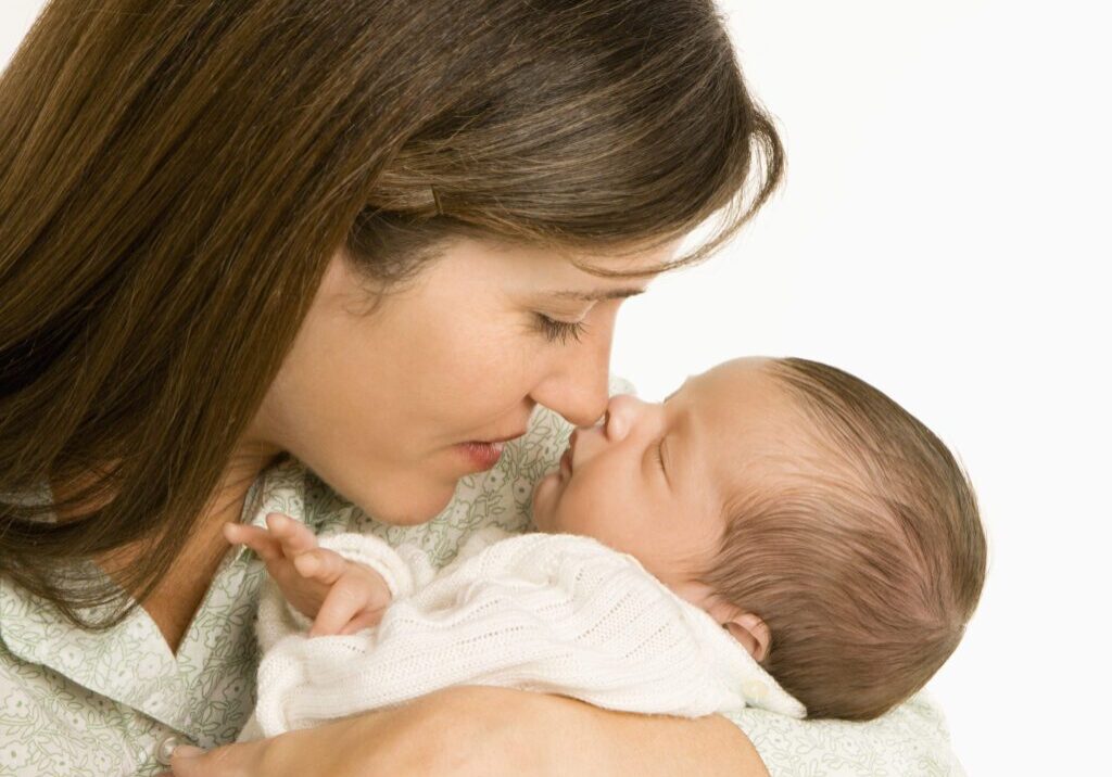 Mother nuzzling sleeping baby with nose and smiling.