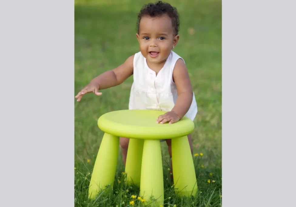 Smiling baby girl standing by green stool.