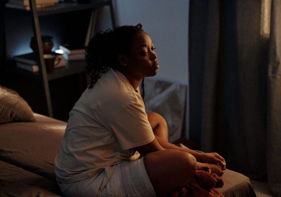 Young troubled woman sitting on bed and looking aside while reminiscing good times and people connected with that period of her life