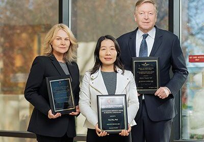 Three people holding awards in suits.